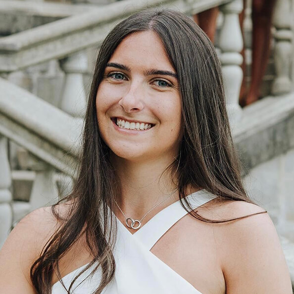 Madison Povemba, dressed in white, and smiling at the camera after convocation.